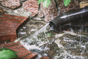 Summer shower. A strong stream of water flows out of the downspout drainpipe in the yard