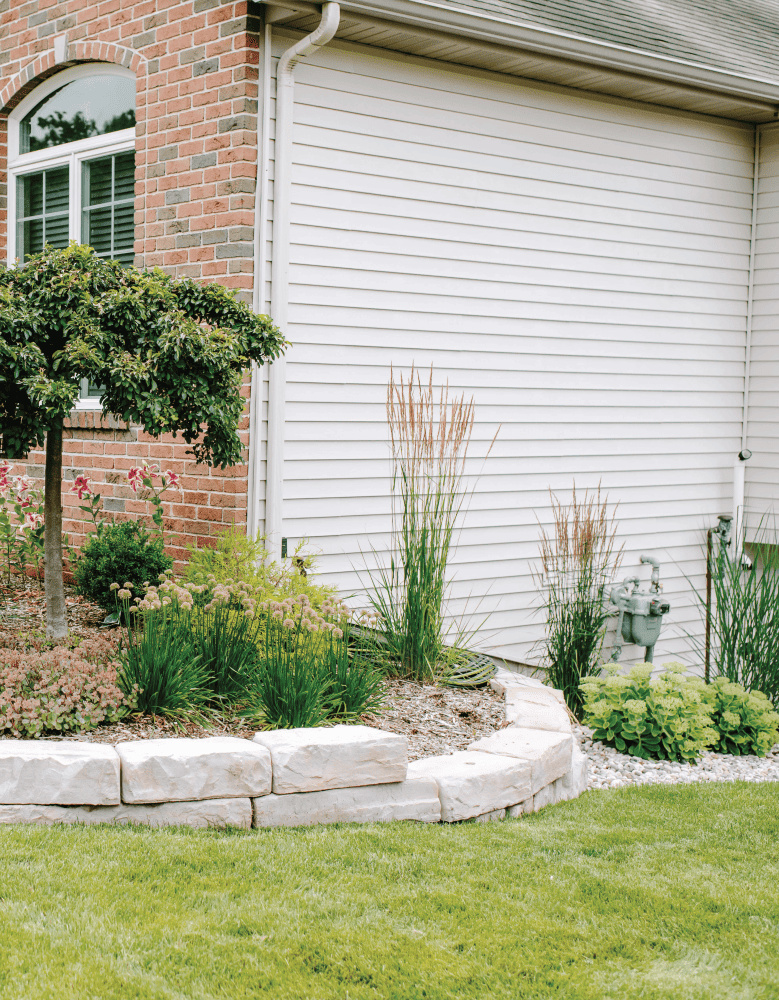 Low Maintenance Landscaping project done by Torchwood Landscaping in Ada, MI. Photo is of landscaping in front of the house and alongside of the house, leading to the backyard.