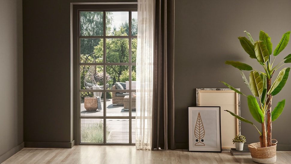 Grey room with window frame and wicket chair, curtain vase of plant.