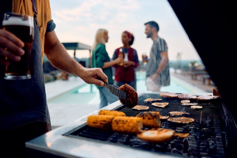 Close up of man making barbecue at poolside party in backyard.