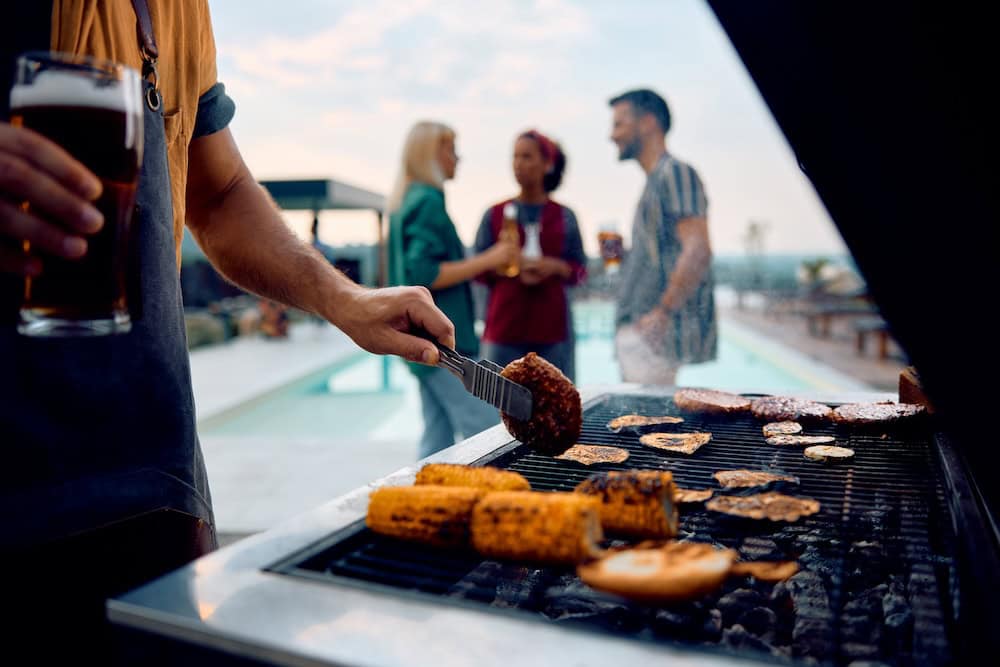 Close up of man making barbecue at poolside party in backyard.