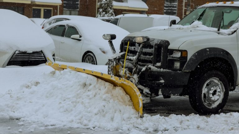 During heavy snowfall, snowplow truck removes snow from parking lot